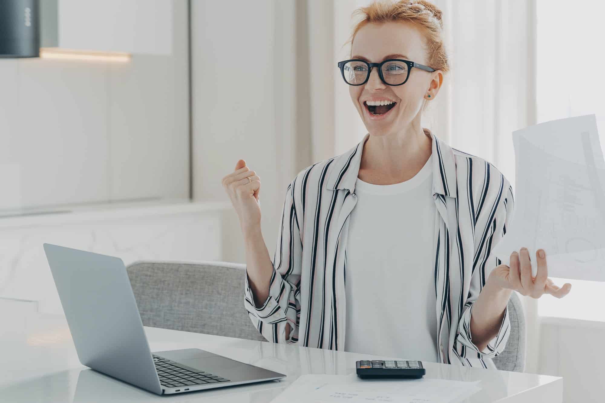 Overjoyed ginger woman holds papers works on project statistics celebrates finishing of work